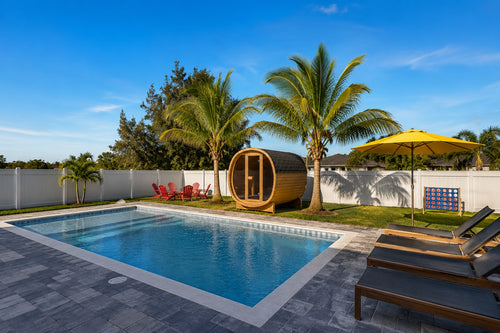 Luxury Cape Coral backyard featuring a swimming pool, lounge chairs, tropical palm trees, and a modern outdoor barrel sauna positioned between two palms.