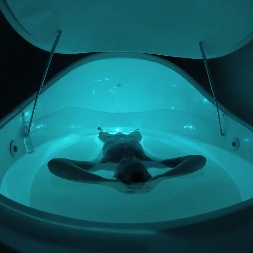 Dreampod V2 flotation tank open with a person floating inside under soft white ambient lighting