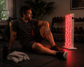 Man using the Helio Cure Helio Glow red light therapy panel after a workout in a home gym to support muscle recovery, reduce soreness, and improve athletic performance.