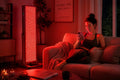 Woman relaxing on a sofa while receiving red light therapy from a full-body panel in a home wellness room.