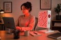 Alt Text: Woman working at a desk while using a Helio Spark red light therapy panel in a modern home office.