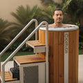 Man using the Icetubs IceBarrel thermowood cold plunge tub with optional stairs and handrails in an outdoor wellness setting.