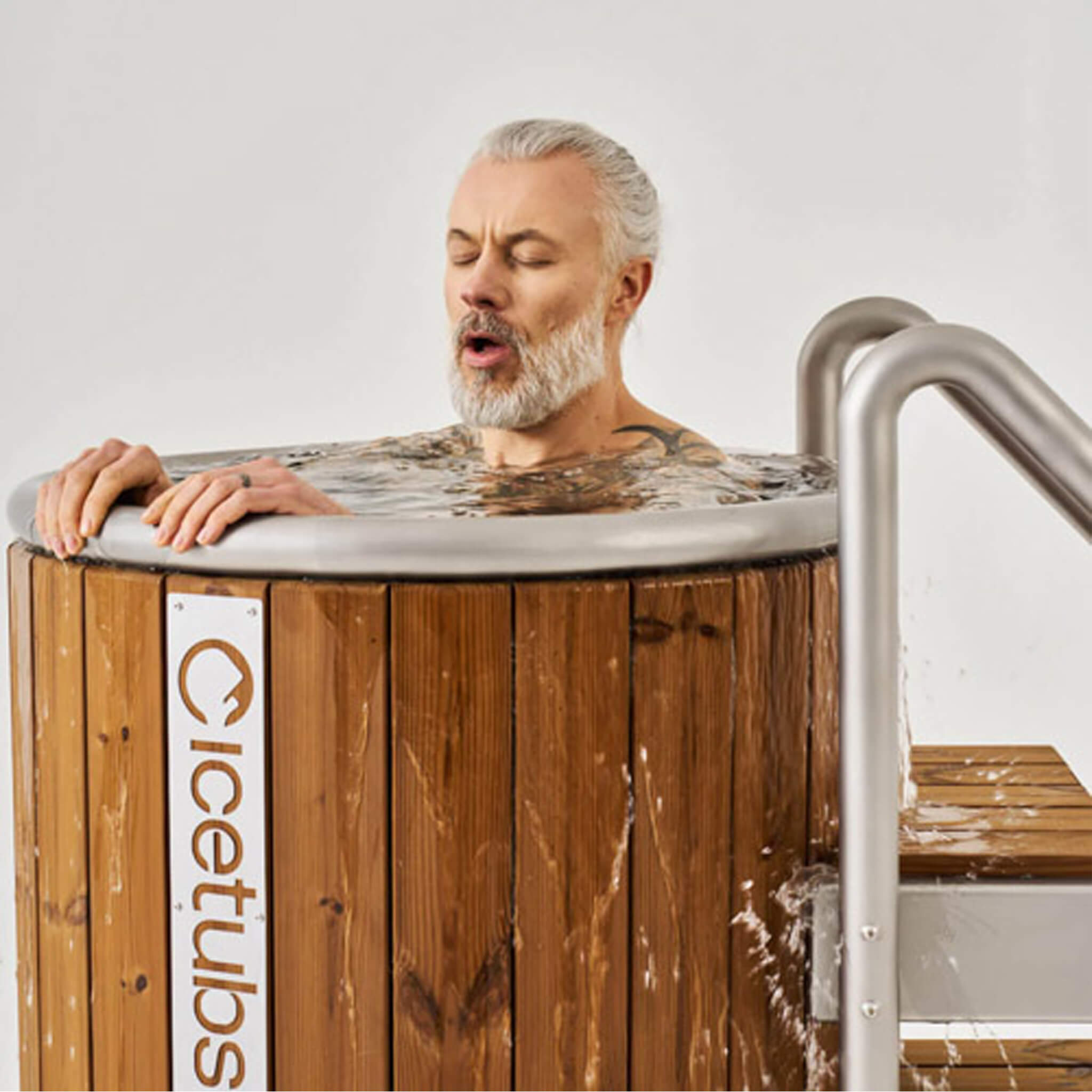 Man using the Icetubs IceBarrel thermowood cold plunge tub with optional handrail system.