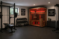 Rövia Ember 4-person full-spectrum infrared sauna installed in a modern home gym with rubber flooring, dumbbells, and squat rack for post-workout recovery.